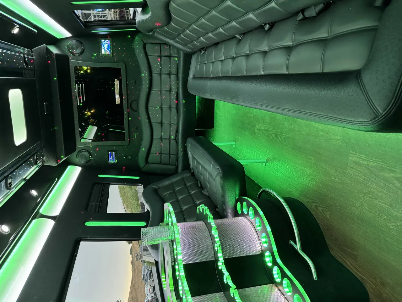 Mercedes-Benz Party Bus interior with perimeter lounge seating, LED accent lighting and wood-look flooring for prom car rental in Burson, CA